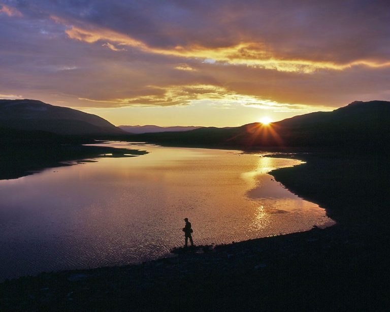 Image of a lake with fishermen standing on the shore and fishing in the evening sun