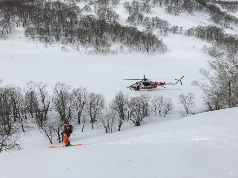 Man on slalom skis going down the mountain and a helicopter stands below