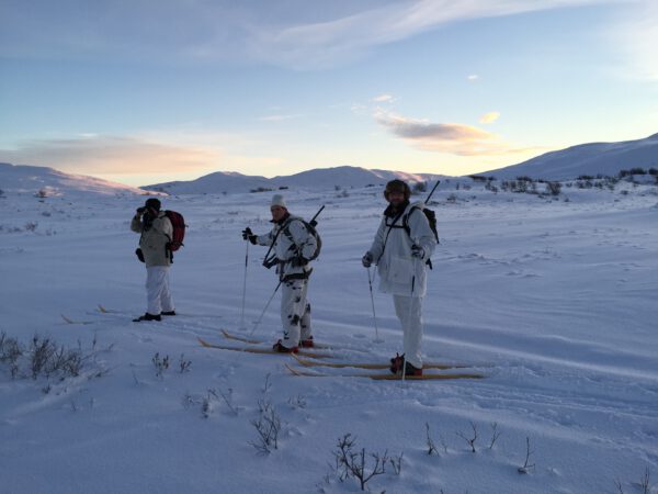 Three white-clad men on skis smiling at the camera