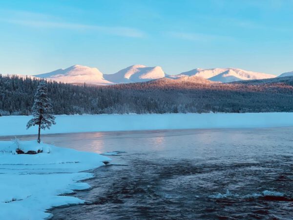 Snow landscape with icy lake and snow-capped mountains on the horizon