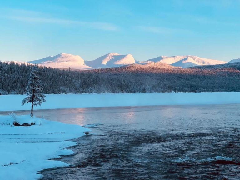 Snow landscape with icy lake and snow-capped mountains on the horizon