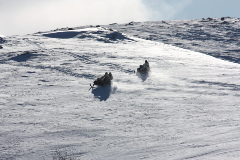 Two snowmobiles heading up the mountain hill